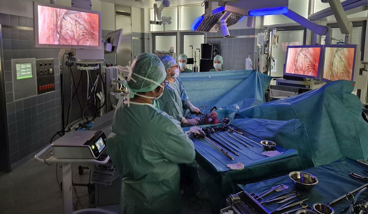 Man sieht einen Operationssaal mit einer Ärztin in einem Arzt in OP-Kleidung während einer Bauch-OP.