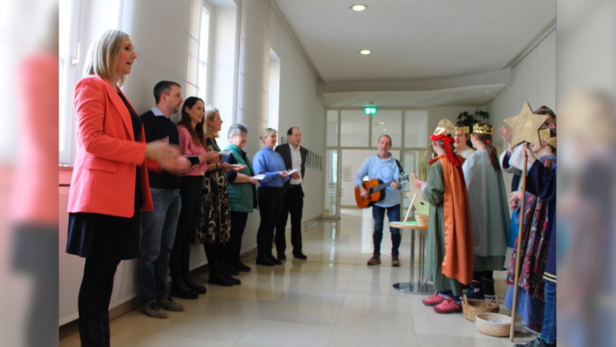 Bild: Die Sternsinger stehen in einem Gang des Bayerischen Kultusministeriums und singen Mitarbeitenden vor.